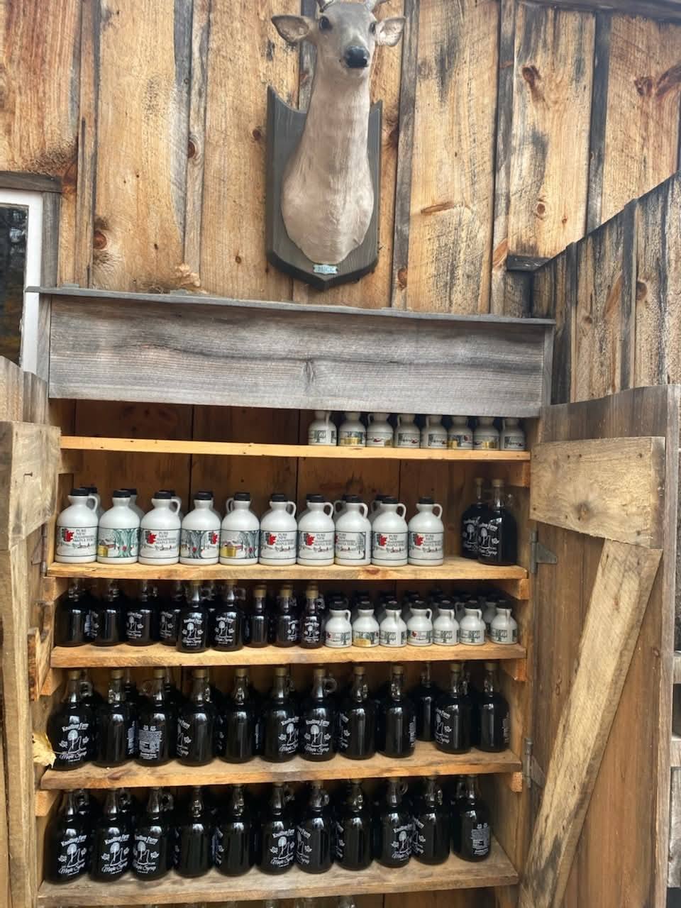 A wooden cabinet filled with maple syrup jugs and glass bottles at the farm